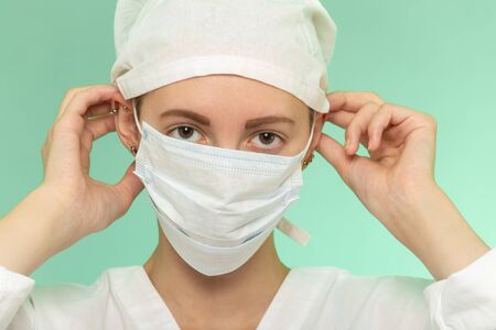 young woman in medical protective mask looking at camera on green background