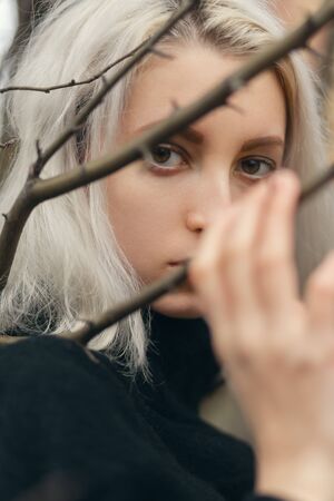 serious young blond woman at dry spring plants looking at cameraの写真素材
