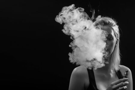 young woman smoking electronic cigarette on black background, monochromeの写真素材
