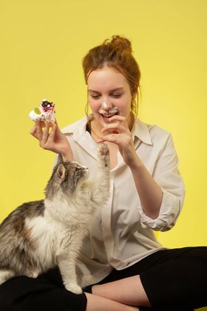 fun pretty red hair girl with cat eats sweet cherry dessert on yellow backgroundの写真素材