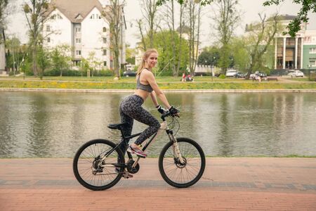 happy blond woman driving on bike in city park near pondの写真素材