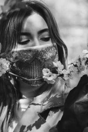 serious young woman with medical protective mask smell spring flowers, monochromeの写真素材