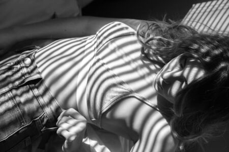 young woman undressing, shows her slim body in sun light with blinds shadows, monochrome