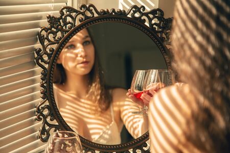 sad single young woman near mirror drinks red wineの写真素材