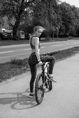 sports slim young blond woman posing with bike on street, monochromeの写真素材