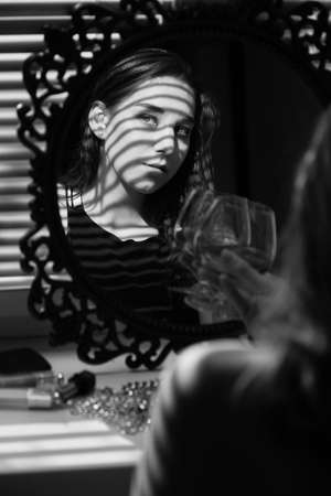 sad single young woman in lingerie drinks red wine in sun light, looking at camera, monochromeの写真素材