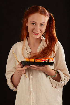 happy red hair young woman with sushi on black background looking at cameraの写真素材