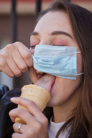 fun young woman with medical mask eats ice cream