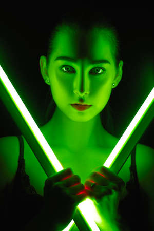 serious young woman in green neon light in dark looking at camera