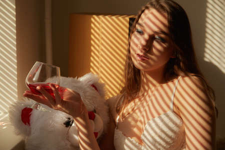 young woman in lingerie drinks red wine with her teddy bearの写真素材