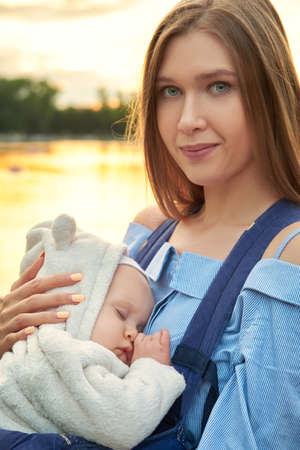 young happy mom with her sleeping baby on hands smiling, closeup portrait