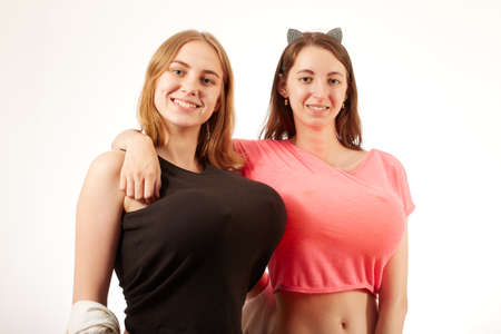 young women showing their big fake breasts on white background, looking at camera, smilingの写真素材