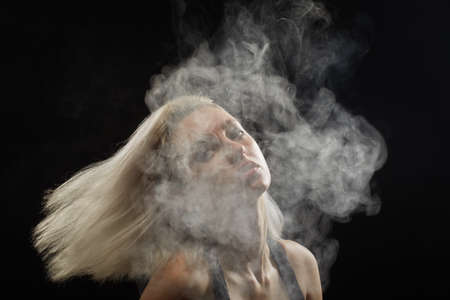 young blond woman dancing in white smoke cloud on black background