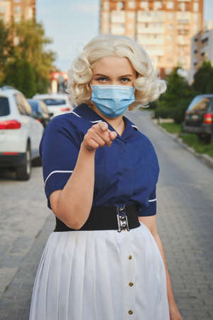 young blond woman in medical mask on street point at cameraの写真素材