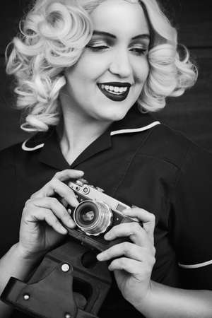 young blond woman with old-style photo camera smiling, monochrome