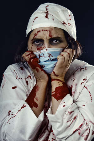 gloomy bloody woman doctor on a black background looking at cameraの写真素材