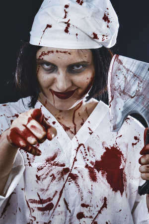 gloomy bloody woman doctor with an ax on a black background point at cameraの写真素材