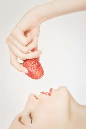 young woman eats juicy strawberry on white background closeup side viewの写真素材