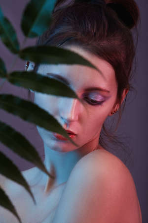 serious young woman cover her face with tropical leaf looking downの写真素材