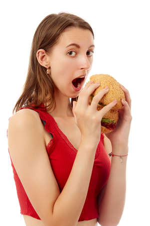 happy young woman eats cheeseburger on white background isolated looking at cameraの写真素材