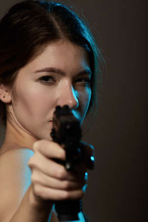 serious young woman with gun aiming at camera, closeup portrait