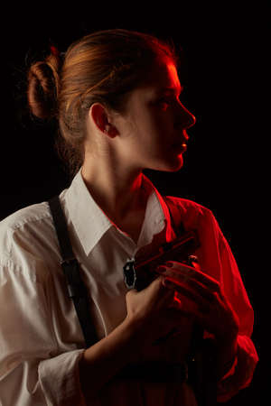 young woman with gun in dark with back red light. Profile silhouette viewの写真素材