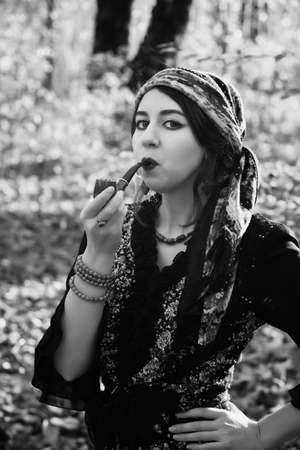 young gypsy woman smoking pipe in autumn forest, looking at camera, monochromeの写真素材