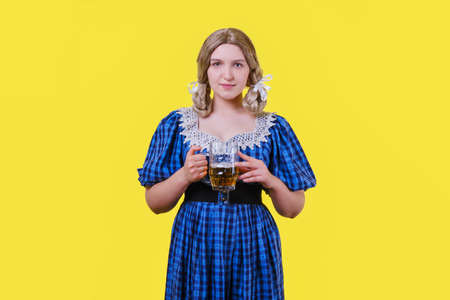 young woman in a blue dress with a mug of beer on a yellow backgroundの写真素材
