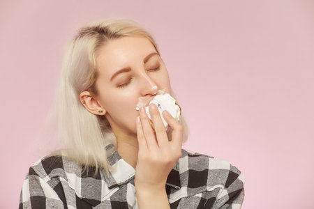 happy pretty blond girl with sweet dessert on pink background overeats it with closed eyesの写真素材