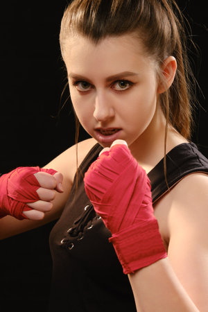 Muay Thai female boxer in attack pose. Fitness young woman boxing training on black background