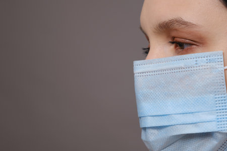 young woman in medical mask looking aside closeup image on gray background, profile viewの写真素材