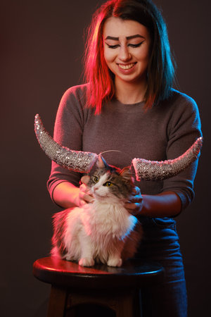 Taurus Zodiac Sign. Astrology and horoscope concept, young woman plays with cat and horns in multicolor light on dark backgroundの写真素材