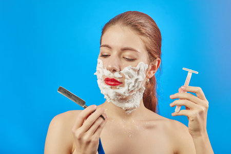 fun young woman has shave with razors on blue backgroundの写真素材
