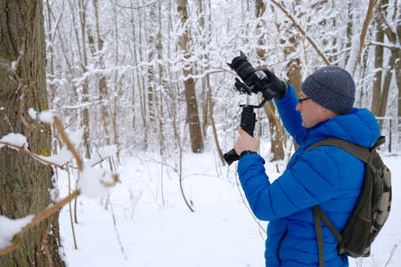 professional cameraman with camera taking shoots in snow forestの写真素材
