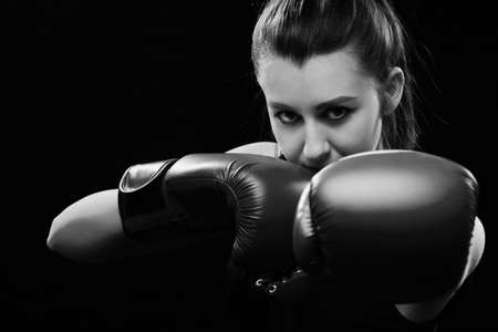 Angry Muay Thai female boxer in attack pose. Fitness young woman boxing training on black...