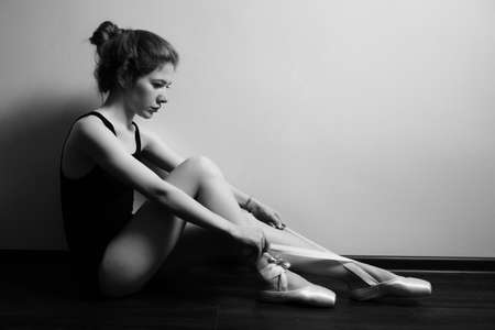 young ballerina feet wear pointes sitting on a wooden floor, monochromeの写真素材