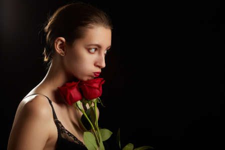 beautiful young woman in lingerie with red roses, natural beauty makeup and bare shoulders closeup on black backgroundの写真素材