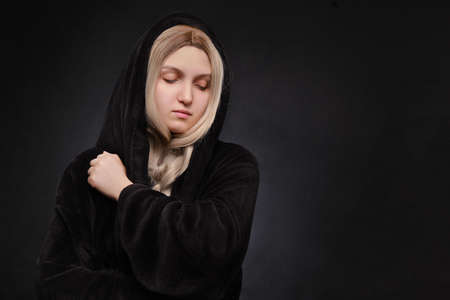beautiful blond young woman in black hood looking down on black background with copy spaceの写真素材