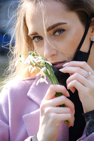 young blond woman with medical mask and snowdrop bouquet at spring timeの写真素材