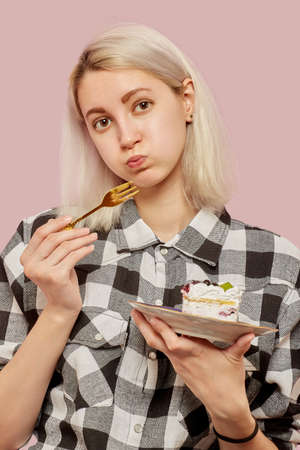 shy pretty blond girl with sweet dessert on pink background looking at cameraの写真素材
