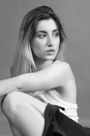 young sad woman in white shirt posing on gray background, monochrome
