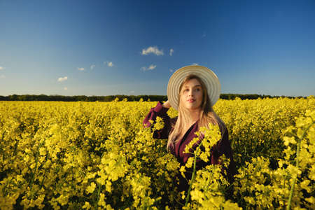 happy young attractive woman in hat and purple dress on rapeseed fieldの写真素材