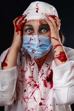 gloomy bloody woman doctor on a black background looking at cameraの写真素材