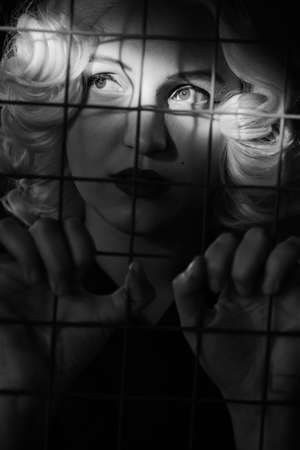 sad scared blonde behind bars close up portrait, monochromeの写真素材