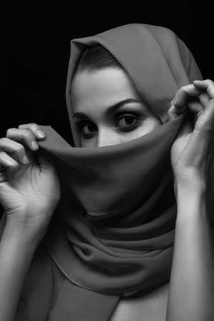beautiful young woman with gray headscarf cover her face with luxury makeup on black background looking at camera, monochromeの写真素材