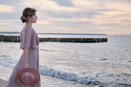 young luxury woman in dress with straw hat near sea looking away profile viewの写真素材
