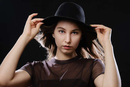 young serious woman in black hat looking at camera on black background