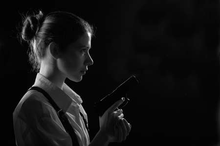 young woman with gun in dark with back red light. Profile silhouette viewの写真素材