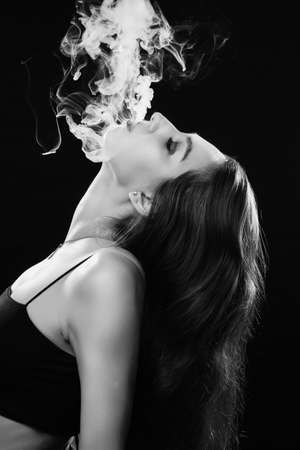 woman with closed eyes blowing smoke on black background, monochromeの写真素材