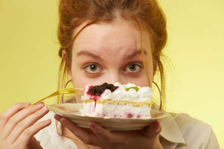 fun pretty curly red hair girl with sweet dessert on yellow background lick lips